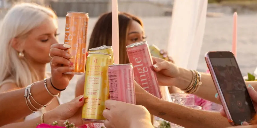 Non-alcoholic drinks mocktail toast with friends holding up assorted Mingle Mocktails cans at an outdoor gathering.