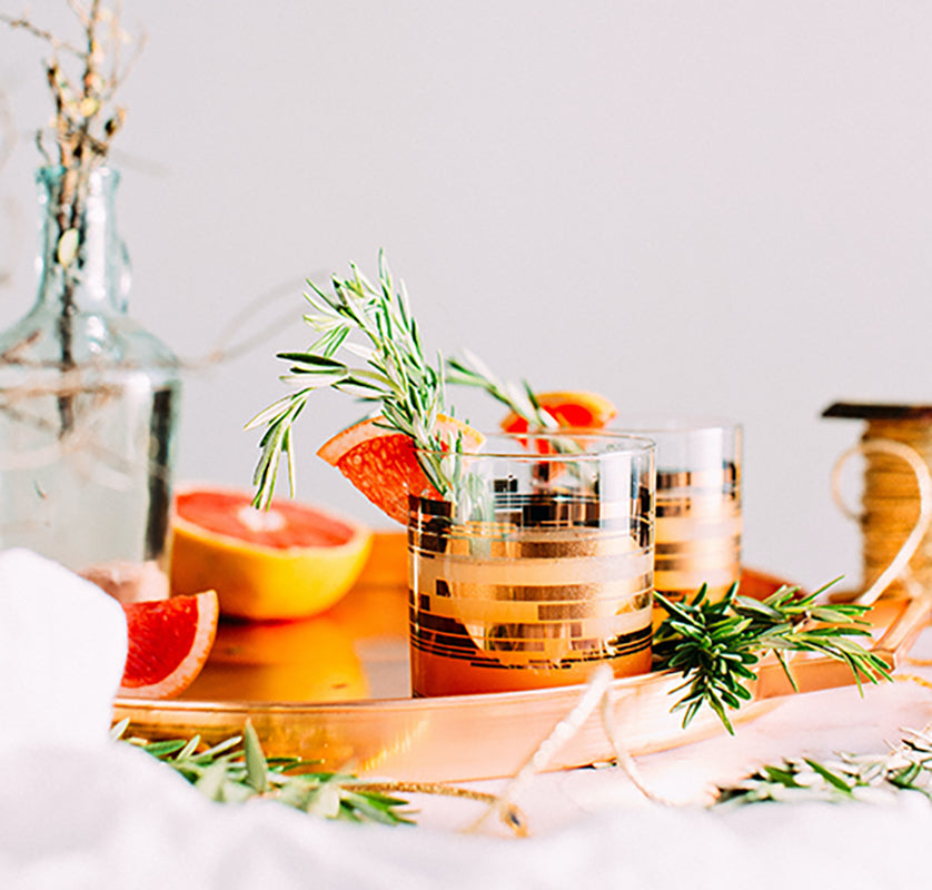 Orange Creamsicle mocktail served in a gold-accented glass, garnished with rosemary & grapefruit slices, placed on a copper tray