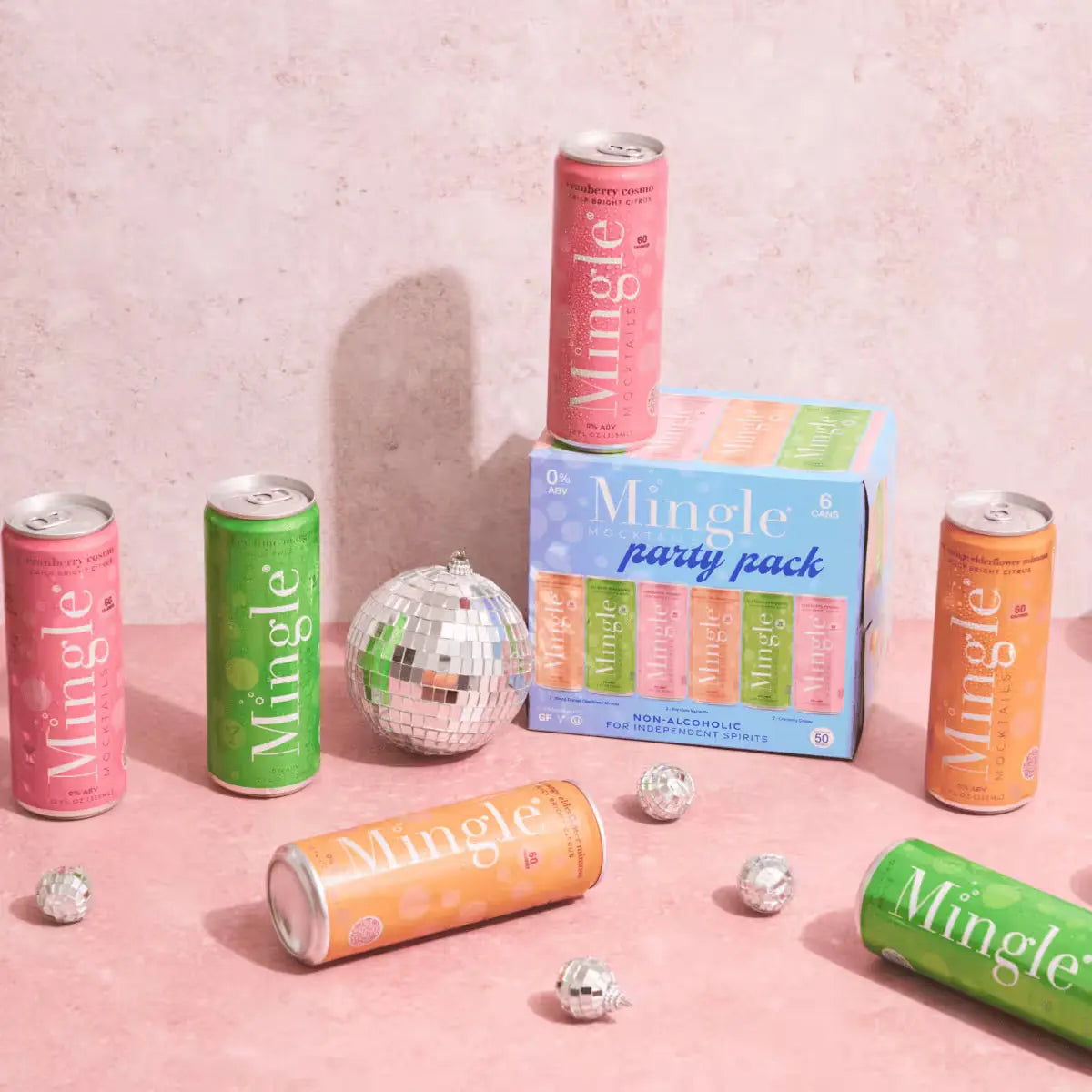 Ready-to-drink canned mocktails from Mingle Party Pack arranged with disco balls on a pink surface.