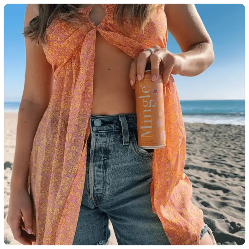 orange mimosa mocktail being held by a woman on a sunny beach.