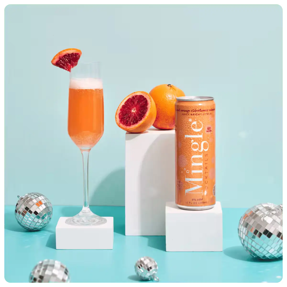 Mimosa mocktail can next to a flute glass with orange garnish and fresh blood oranges on display.