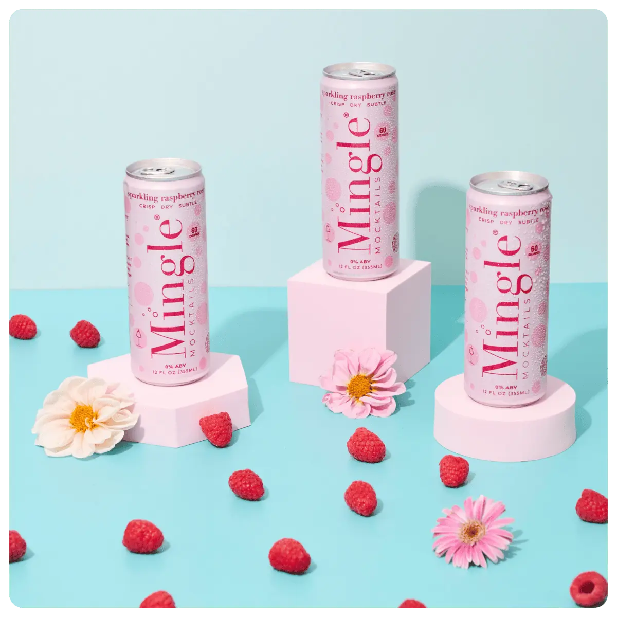 raspberry rosé mocktails being poured into a glass, with cans, fresh raspberries, and flowers arranged on a blue surface