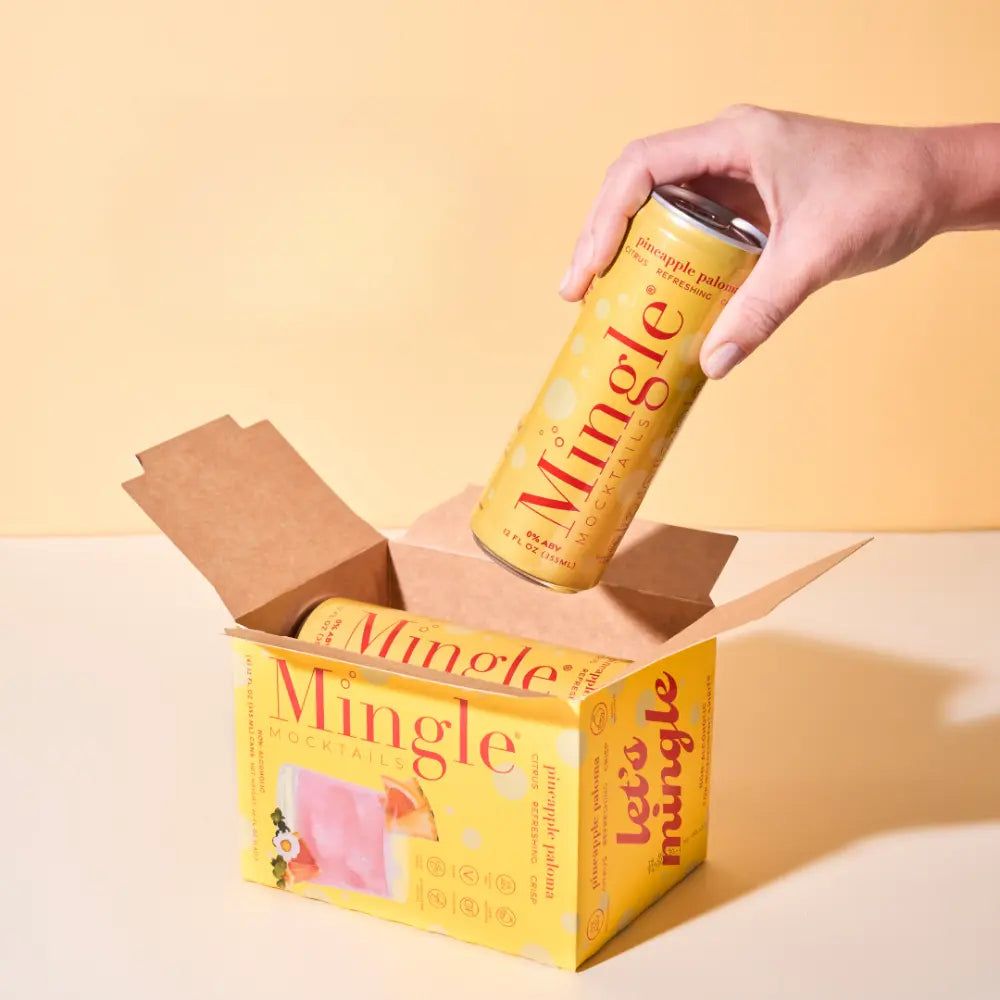 Canned pineapple paloma mocktail being taken from a bright yellow Mingle Mocktails box against a soft yellow background.