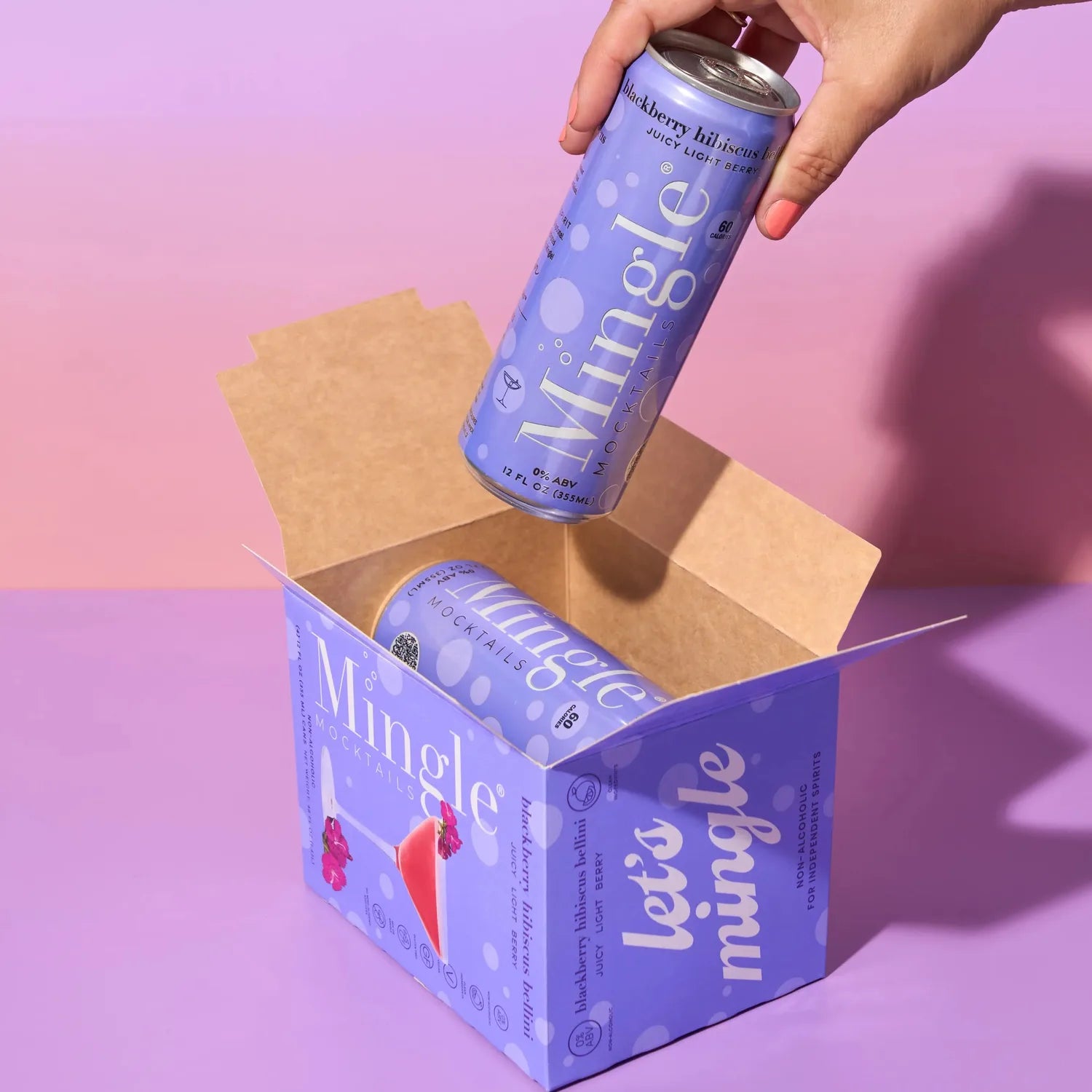 Hand pulling a Mingle Mocktails Blackberry Hibiscus Bellini can from a branded lavender shipping box on a purple background.