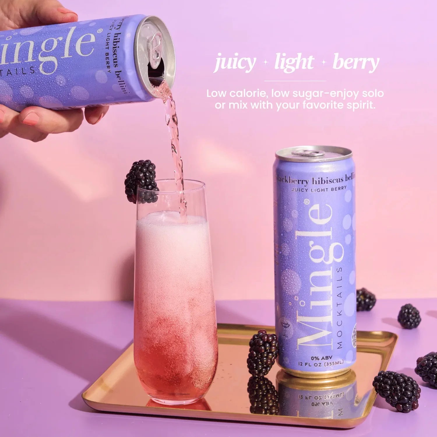 Mingle Mocktails Blackberry Hibiscus Bellini being poured from a lavender can into a flute glass with blackberry garnish on a gold tray.