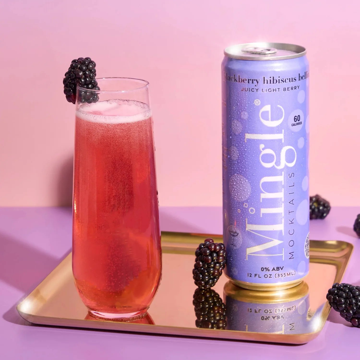 Mingle Mocktails Blackberry Hibiscus Bellini lavender can beside a ruby-pink bellini in a flute glass on a gold tray with blackberries.
