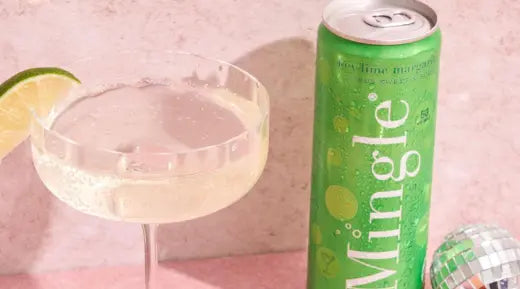 Key lime margarita mocktail in a coupe glass garnished with lime, next to a can of Mingle's key lime flavor