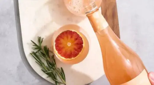 Blood orange mocktail being poured into a glass, garnished with fresh rosemary & a slice of blood orange