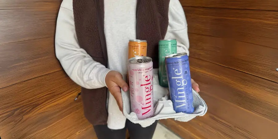 Mocktails assortment in hand featuring four Mingle can flavors against a wooden background.