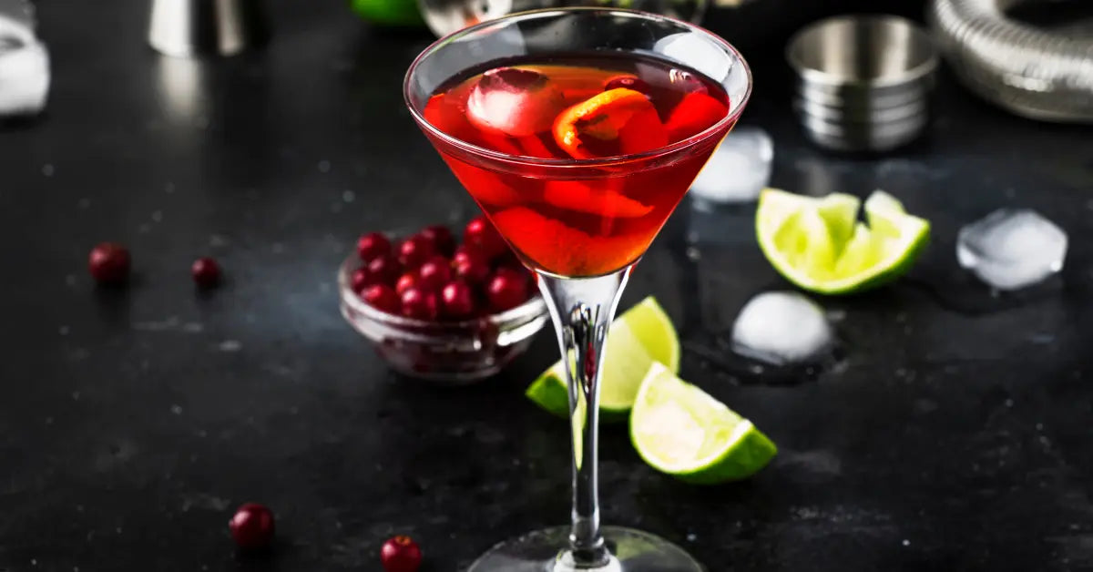 Cranberry mocktail served in a martini glass with fresh cranberries & lime wedges on a dark background