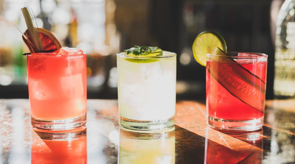 Alcohol-free cocktails garnished with citrus, herbs, & cucumber slices, displayed in glasses on a reflective bar counter