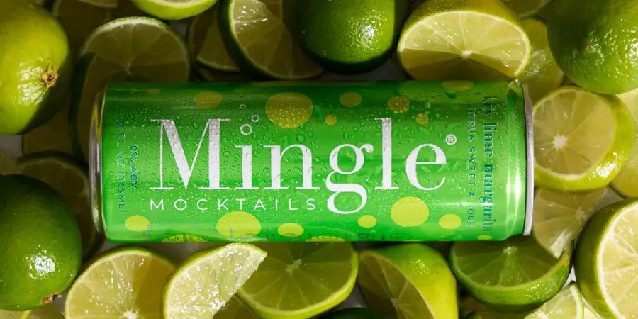 Key Lime Margarita mocktail can from Mingle Mocktails surrounded by fresh-cut and whole limes on a vibrant green citrus backdrop.