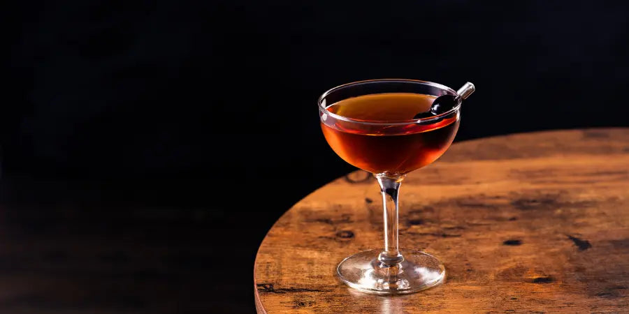  Manhattan mocktail in a coupe glass, garnished with a cherry on a skewer against a dark wooden table