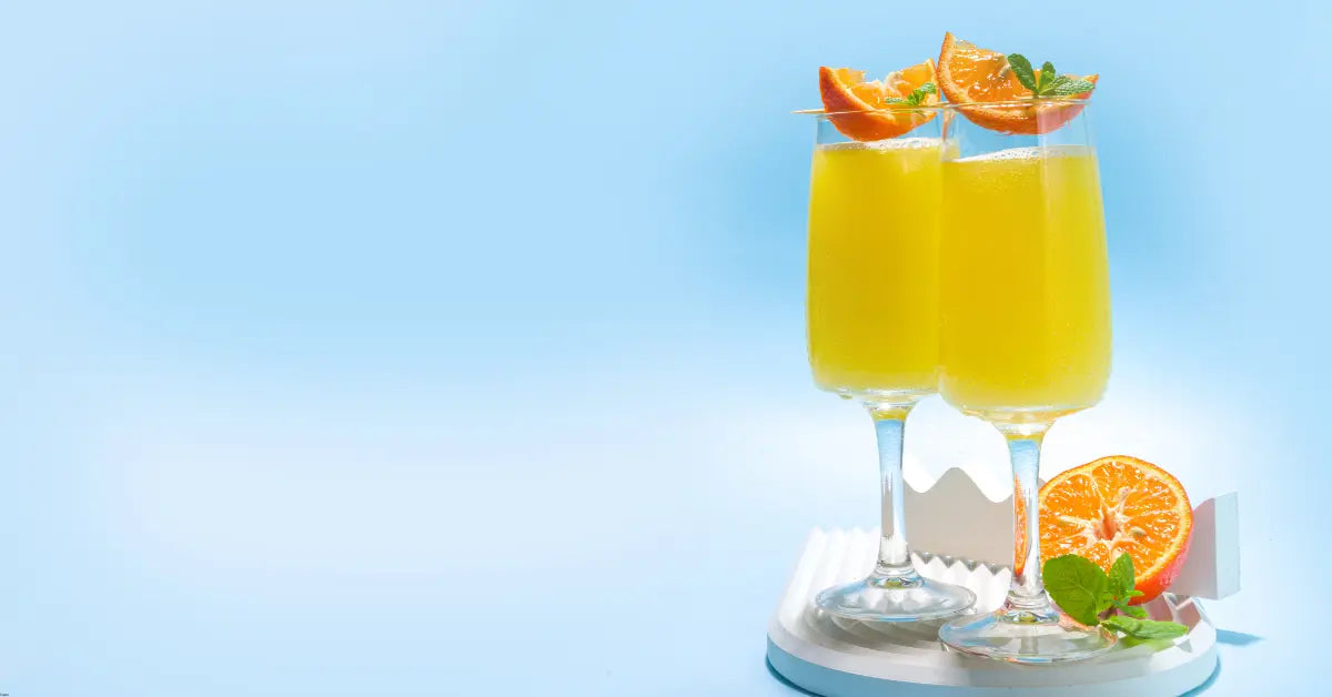Mimosa mocktail served in champagne flutes, garnished with orange slices and mint leaves, set against a light blue background
