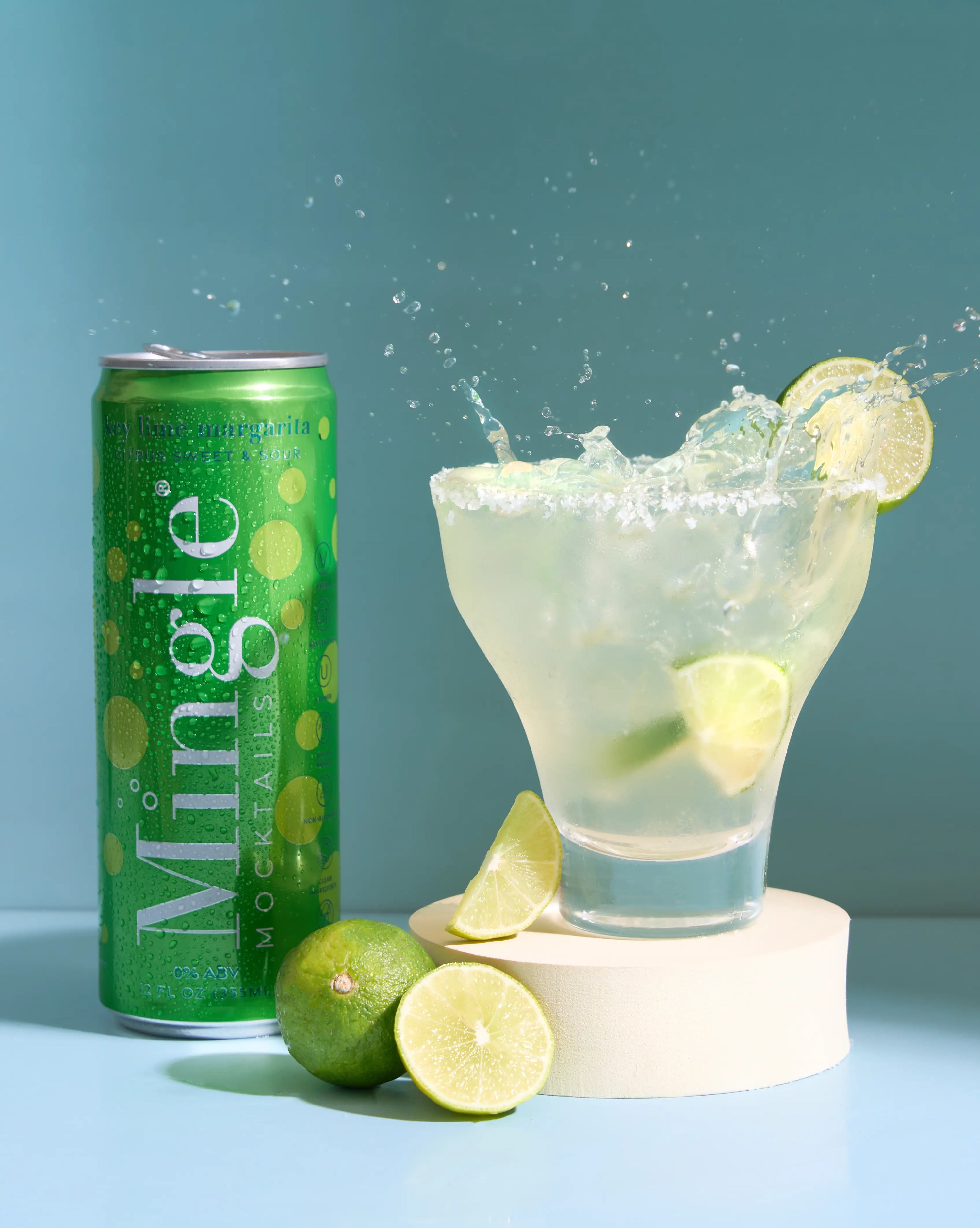 Mingle Mocktails key lime margarita mocktail can alongside a glass with liquid, salted rim, and limes.