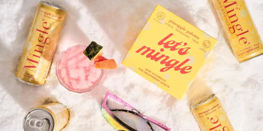 Alcohol-free cocktails featuring Mingle mocktails in pineapple paloma flavor, displayed on snow with a refreshing pink drink and sunglasses.