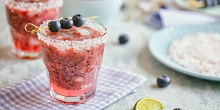 Virgin blueberry mojito served in a glass rimmed with sugar, garnished with a blueberry skewer and ice