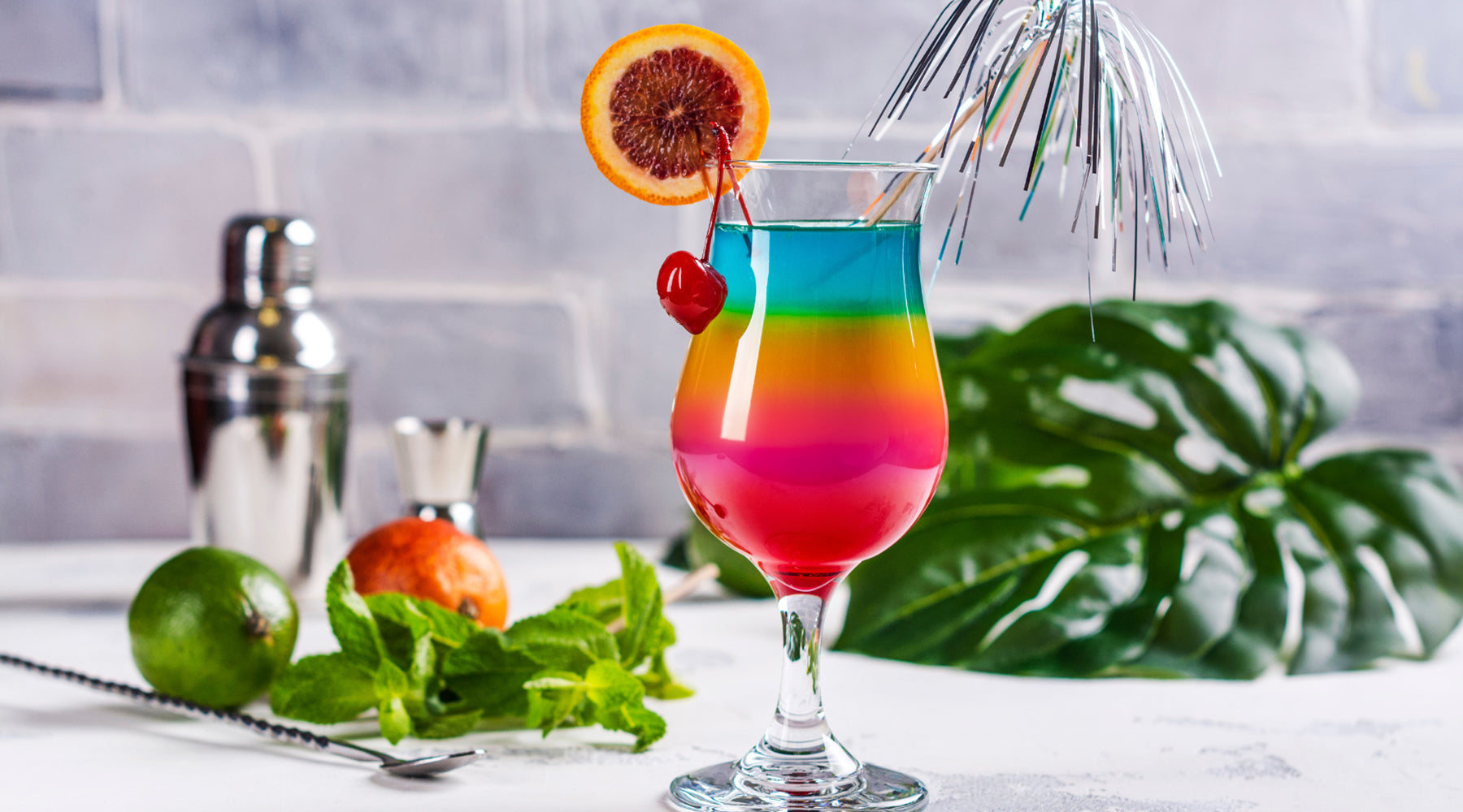 Pride mocktail with vibrant rainbow layers, garnished with a blood orange slice, cherry, & silver decoration