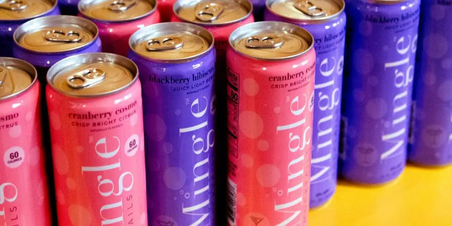 Fresh botanical mocktails from Mingle Mocktails, featuring Cranberry Cosmo and Blackberry Hibiscus Bellini cans arranged on a table.