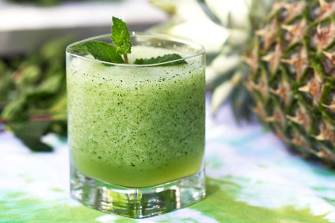 Frozen coconut mojito mocktail garnished with fresh mint leaves, next to a pineapple in a tropical setting