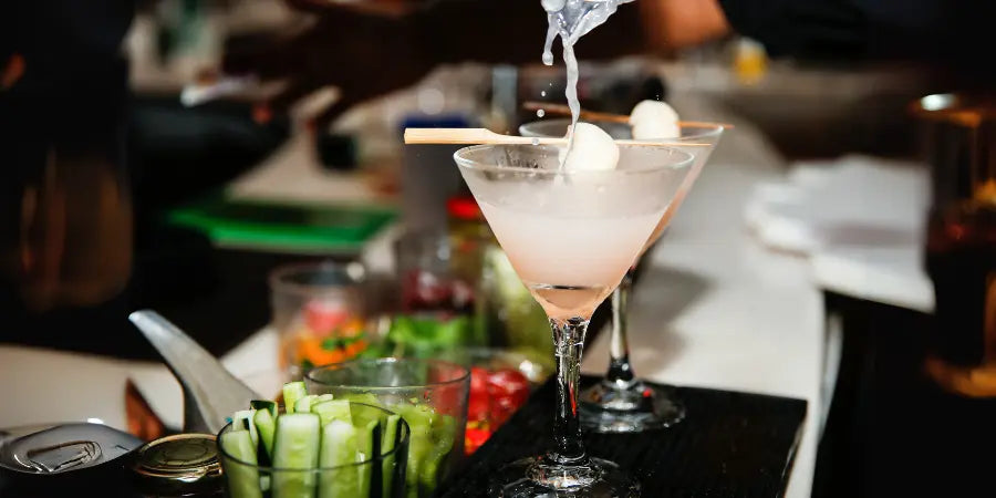 Non-alcoholic lychee martini being prepared at a bar with lychee garnish and pouring action