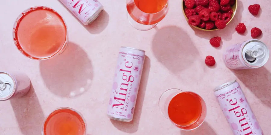 low-calorie mocktails can in various flavors with glasses of sparkling drinks and fresh fruit garnishes on a pink background.