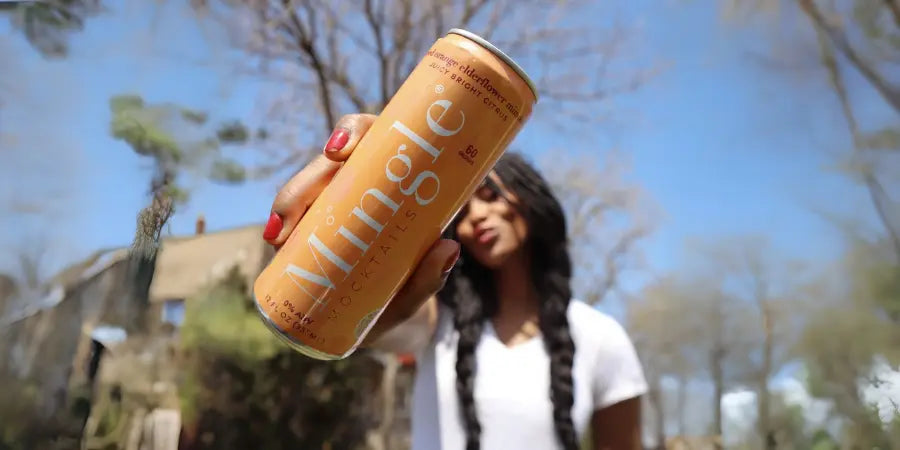Mocktails ready to drink can of Mingle Mocktails shown outdoors by a woman with long braids.