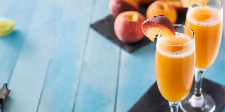 Virgin peach Bellini in flutes on a blue background, garnished with peach slices and surrounded by fresh peaches