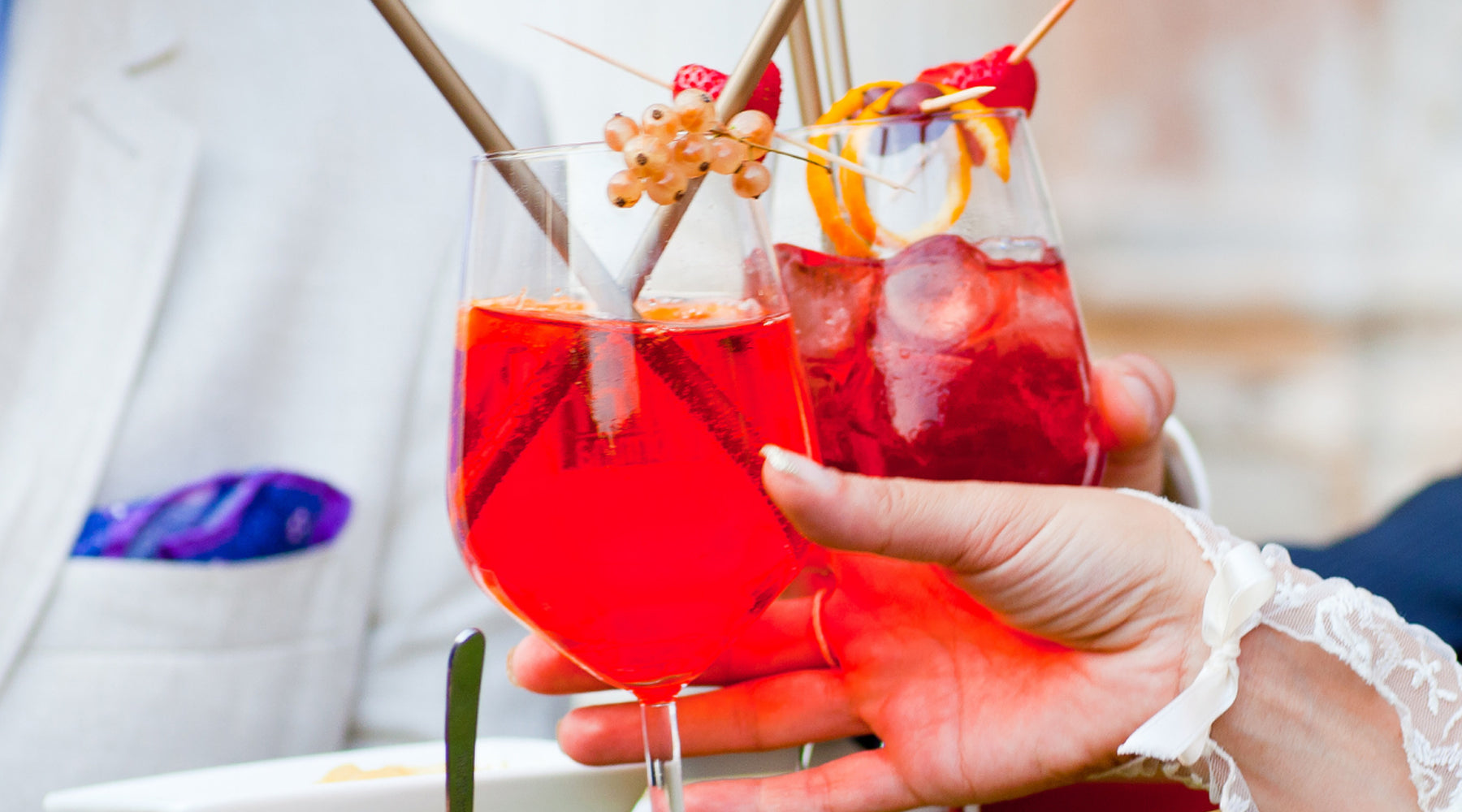 Alcohol-free mocktails for weddings featuring red berry spritzers in stemmed glasses, garnished with raspberries, orange peels, and fancy straws