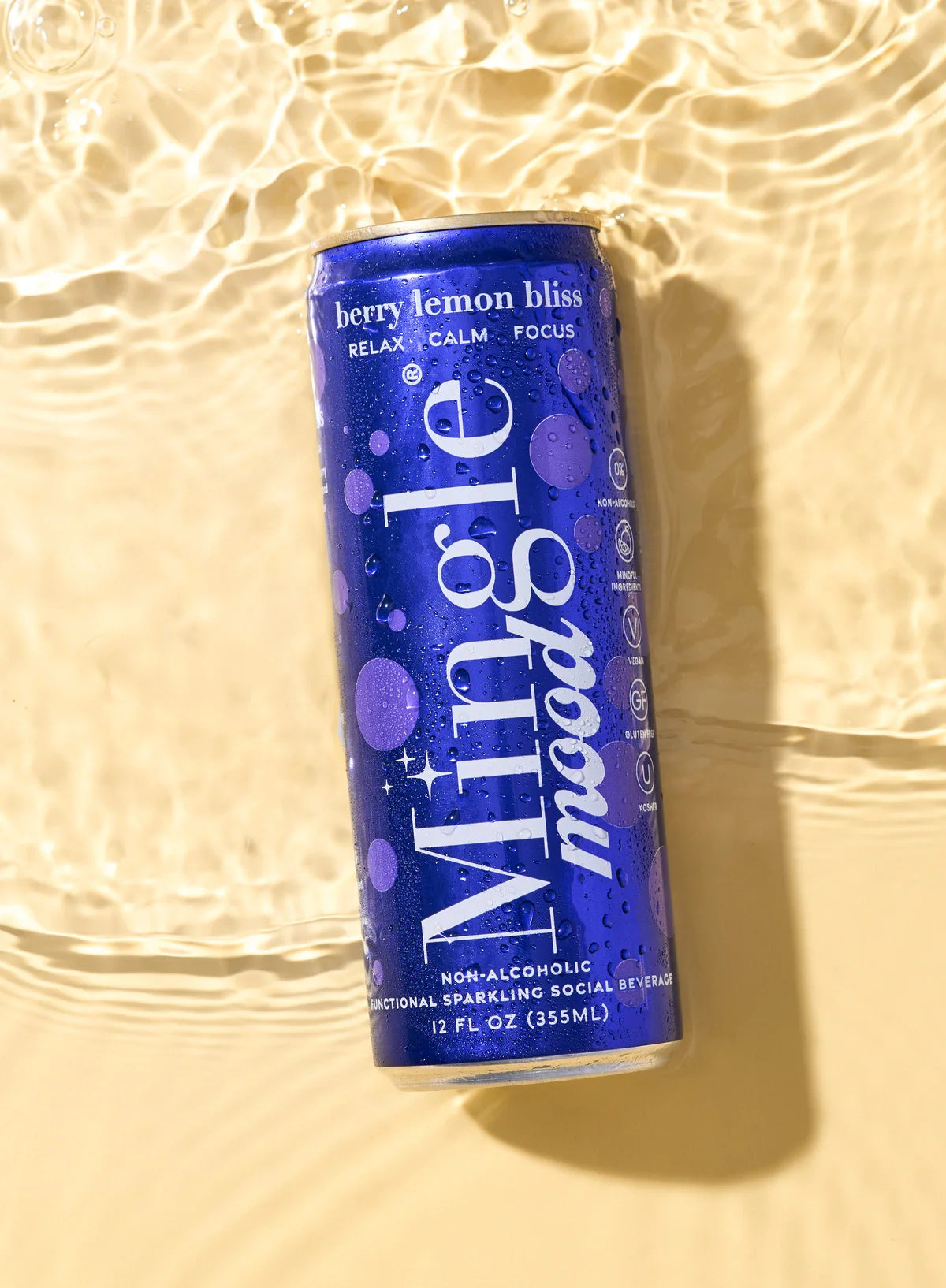 Berry flavored functional mocktail can labeled "Mingle Mood" rests in shallow, sunlit water with refreshing condensation.