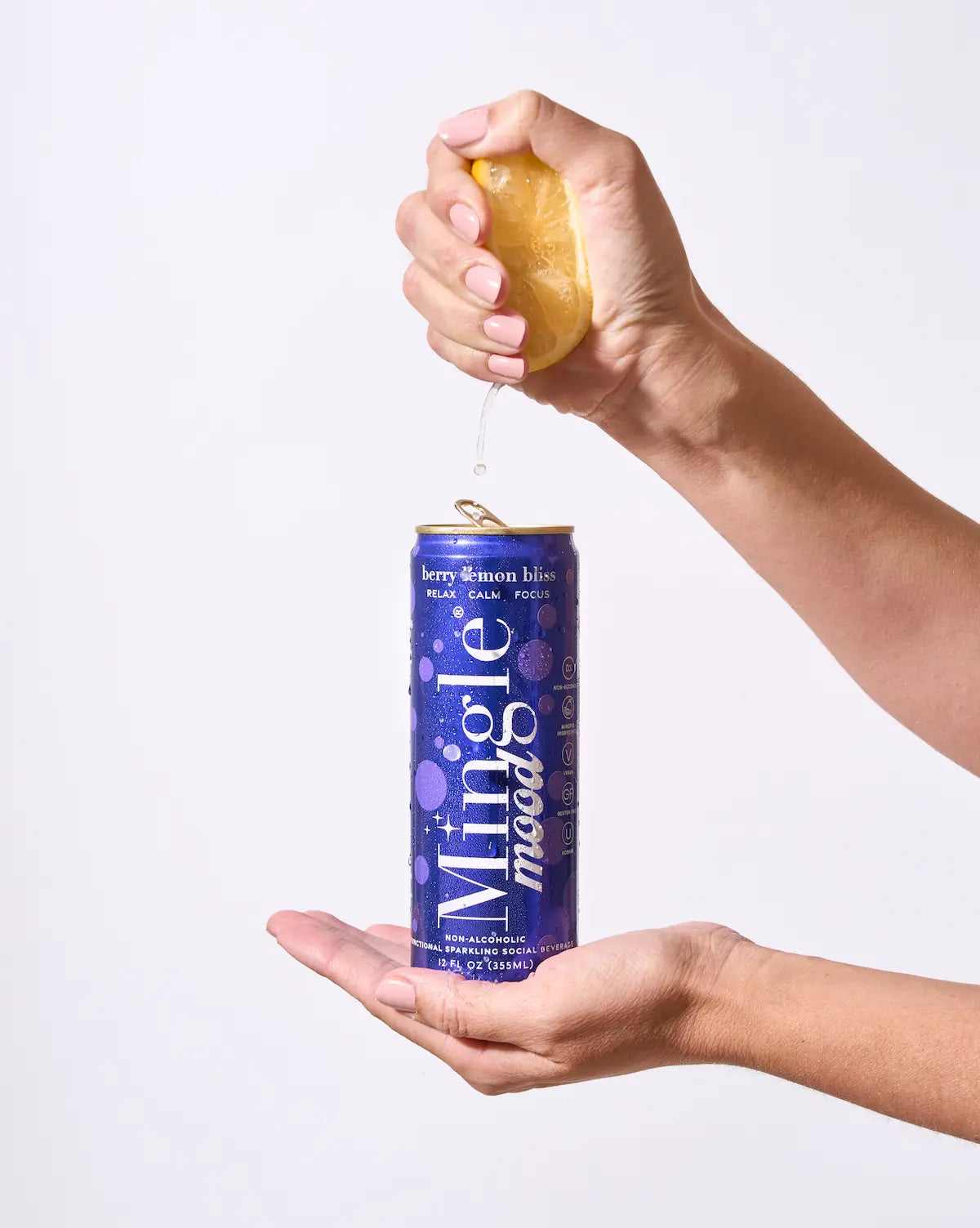 Berry lemon flavored functional mocktail can being held as lemon juice is squeezed over it against a clean white background