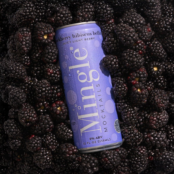 Mingle Mocktails Blackberry Hibiscus Bellini lavender can with condensation resting on a bed of fresh blackberries.