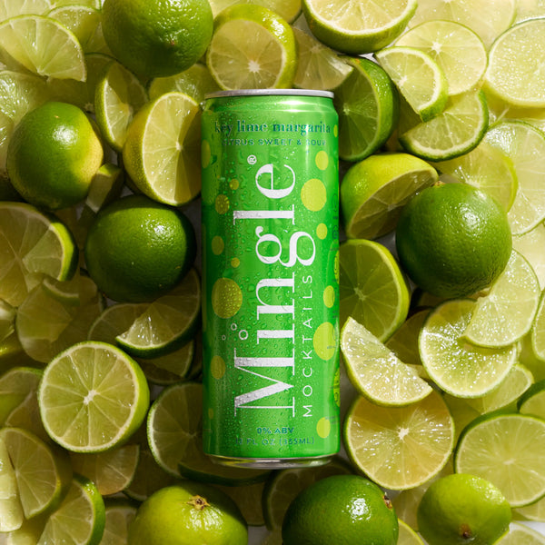 Mingle Mocktails Key Lime Margarita green can with condensation nestled among whole limes and fresh lime slices.