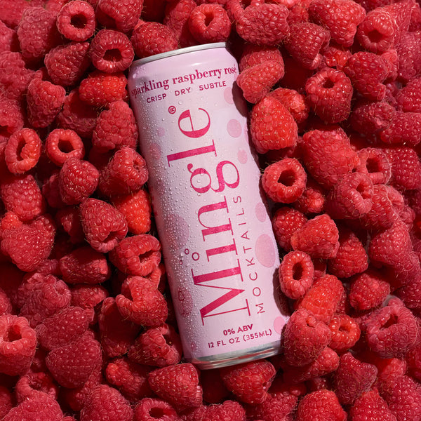 White and pink Mingle Sparkling Raspberry Rosé can with condensation resting on a bed of fresh red raspberries.
