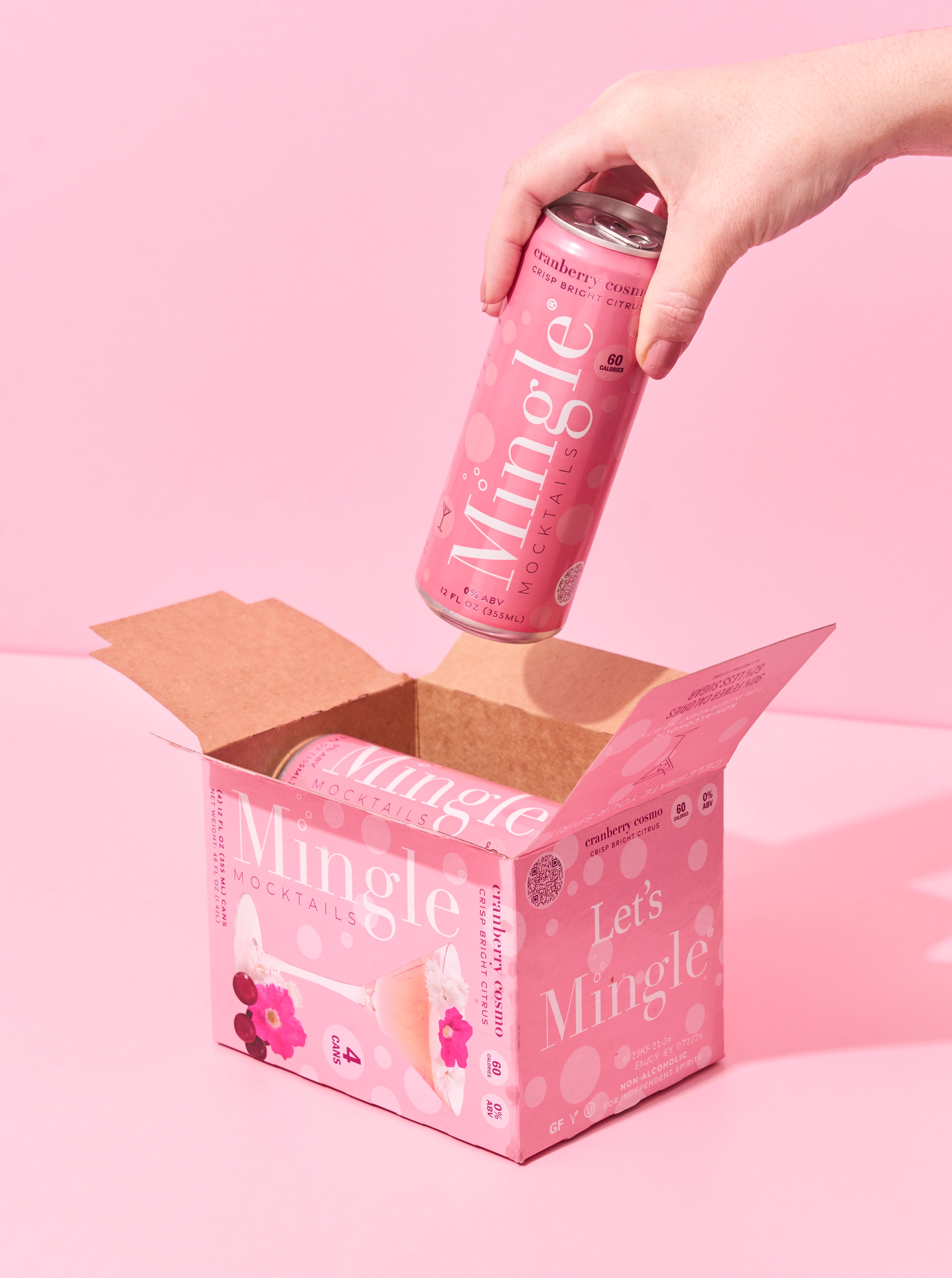 Canned cranberry cosmo mocktail by Mingle, shown in a vibrant pink 12 oz can being lifted from a matching four-pack box, featuring a crisp citrus flavor and 60 calories per serving.