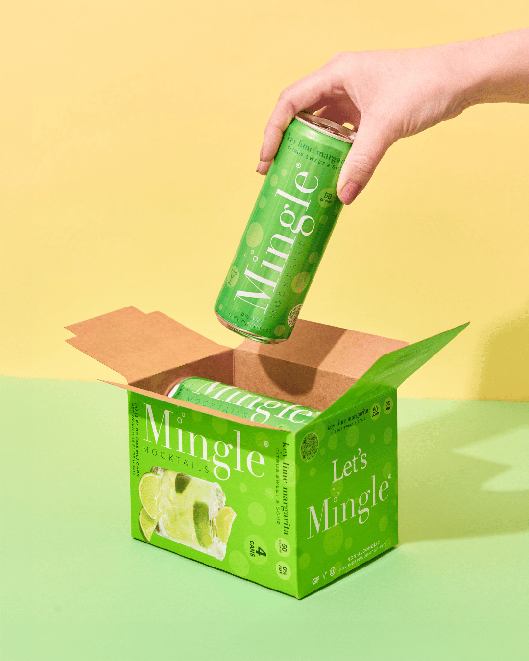 Key lime margarita mocktail by Mingle in a vibrant green 12 oz can, shown being pulled from a 4-pack box, offering a citrusy, sweet and sour alcohol-free drink with only 50 calories.