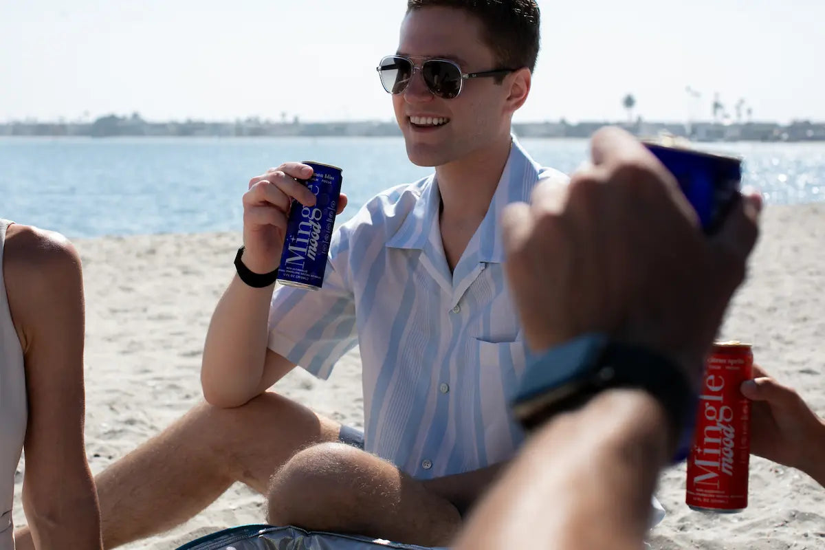 Mocktails with adaptogens enjoyed by friends relaxing on a sunny beach with Mingle Mood cans in hand.