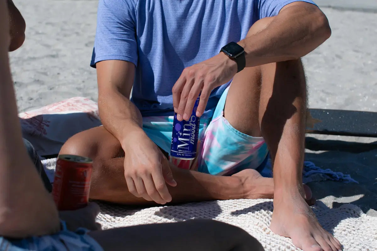 Berry functional mocktail can held by man relaxing on a beach blanket in casual summer clothing.