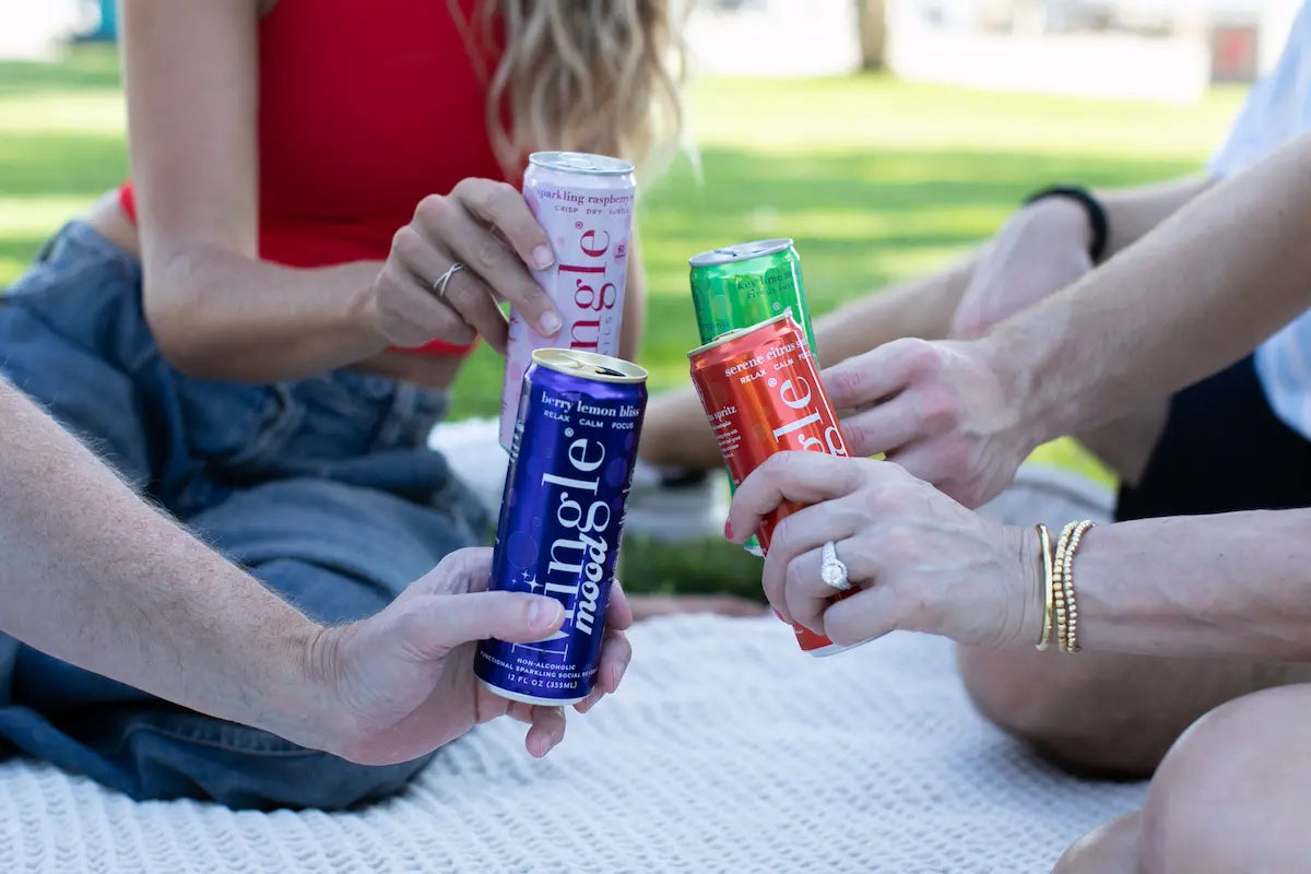 Functional non-alcoholic beverages in colorful Mingle Mood cans being toasted by friends during a casual outdoor picnic.
