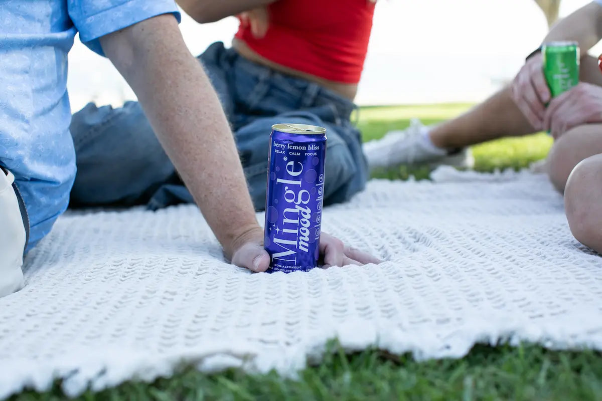 Functional zero-proof beverages like Mingle Mood can enjoyed outdoors on a picnic blanket with friends in a park setting