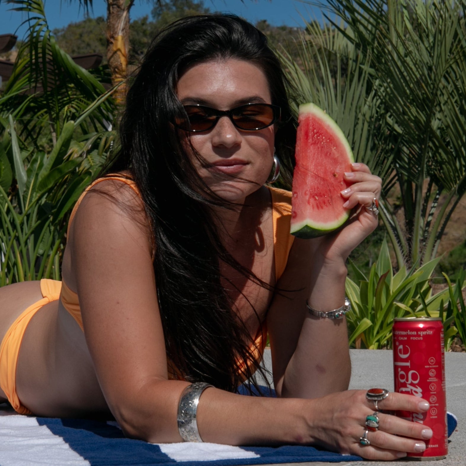 Poolside sunbather holding watermelon slice beside a Mingle watermelon spritz mocktail can.