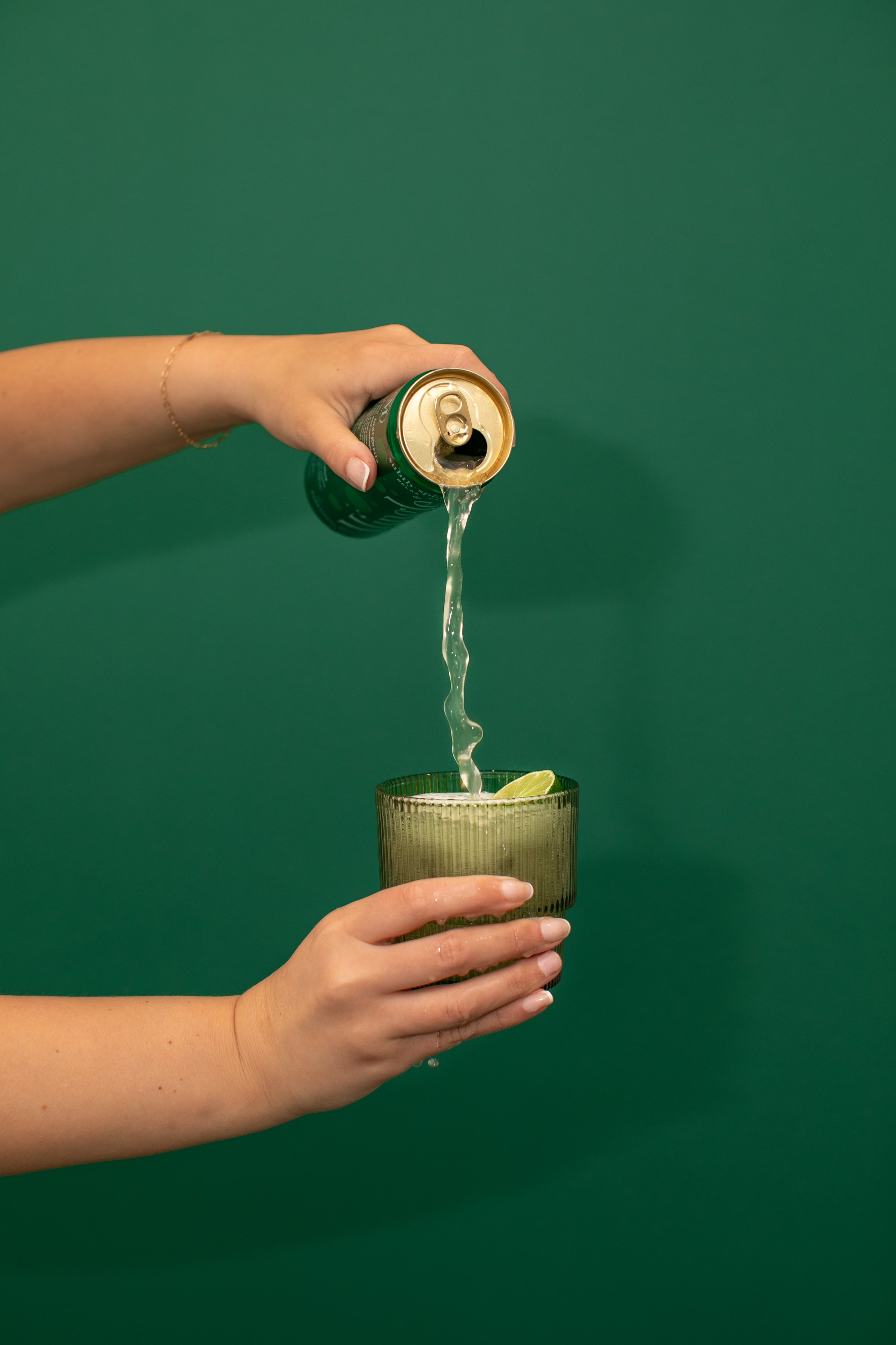 Pouring a canned spicy margarita mocktail into a ribbed glass with lime wedge.