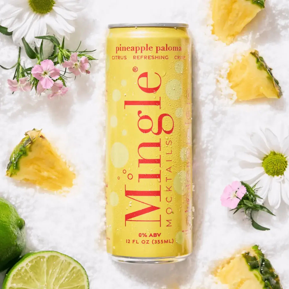 Pineapple Paloma mocktail by Mingle in a bright yellow 12 oz can, surrounded by fresh pineapple, lime, and flowers, offering a crisp, citrusy, and alcohol-free refreshment with 0% ABV.