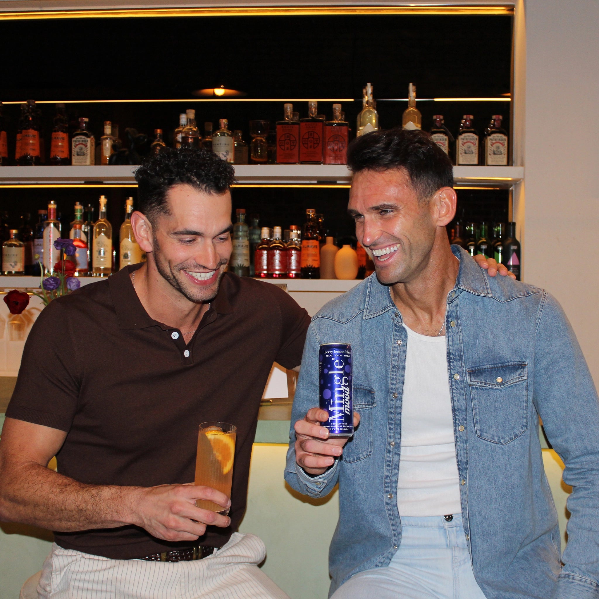 Two friends enjoying Mingle Mood non-alcoholic functional beverages at a bar with cocktail glasses and warm ambient lighting.