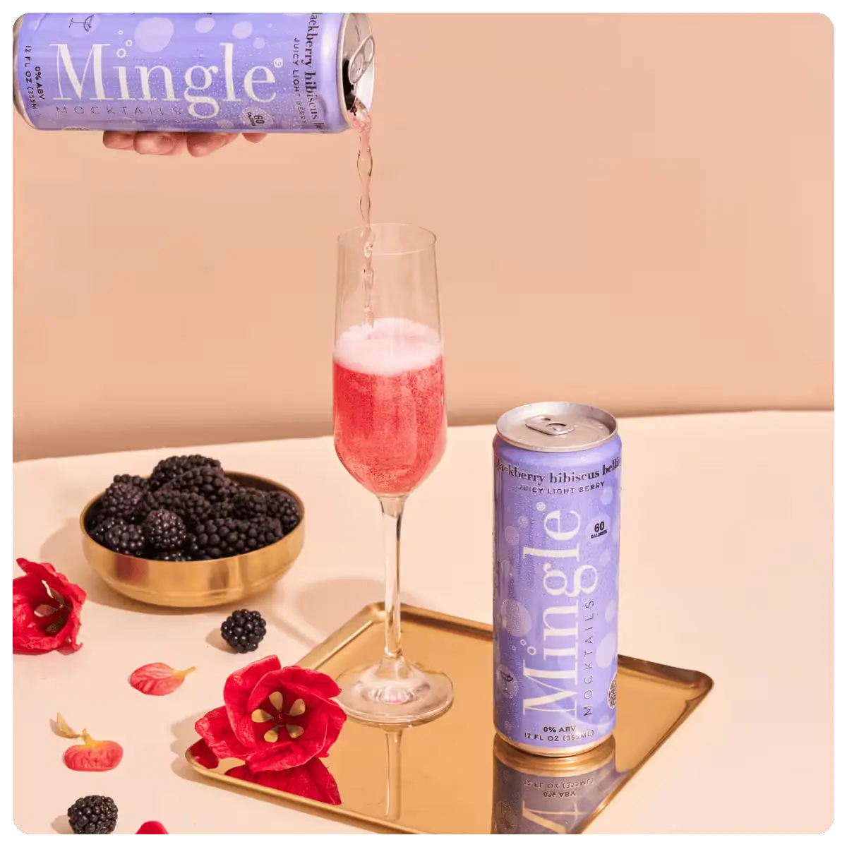 Mingle non-alcoholic blackberry bellini in a champagne flute, accompanied by fresh blackberries and hibiscus flowers.