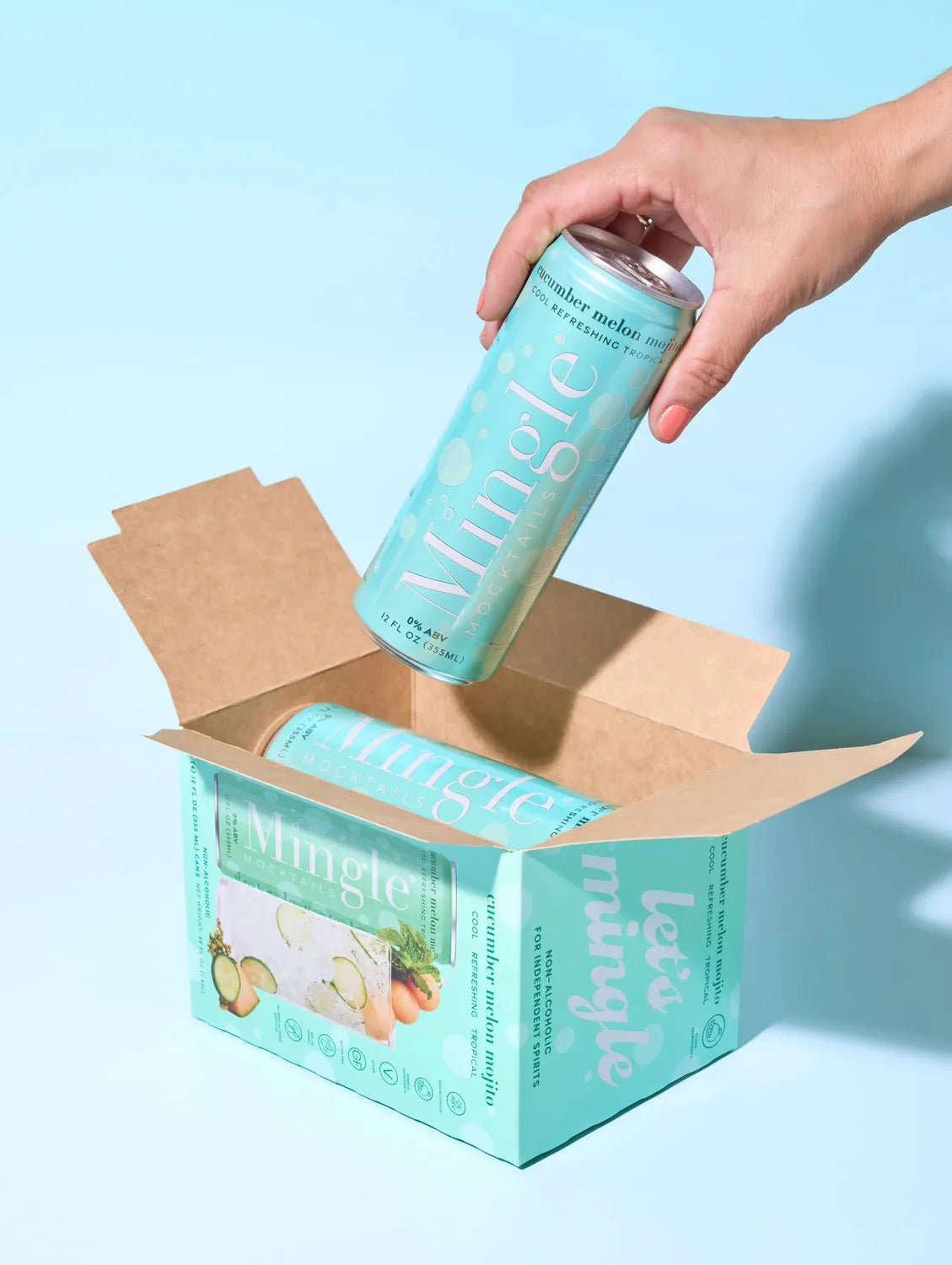 Hand pulling a Mingle Mocktails Cucumber Melon Mojito can from a branded turquoise shipping box on a light blue background.