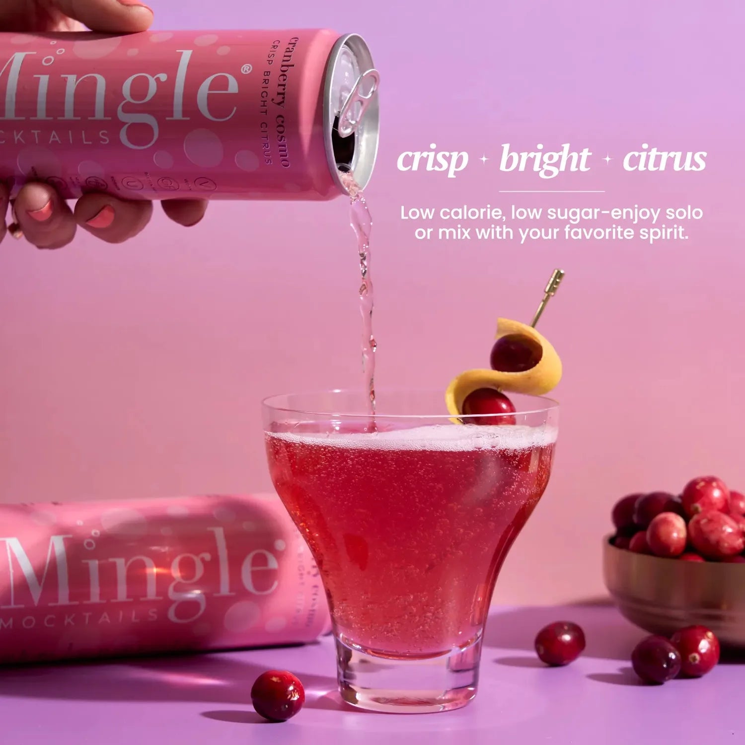 Mingle Mocktails Cranberry Cosmo being poured from a pink can into a cocktail glass garnished with cranberries and a lemon twist.