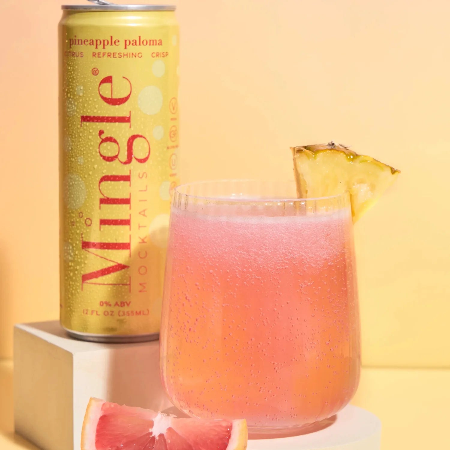 Mingle Mocktails Pineapple Paloma yellow can beside a pink cocktail in a rocks glass with pineapple, grapefruit, and lime.