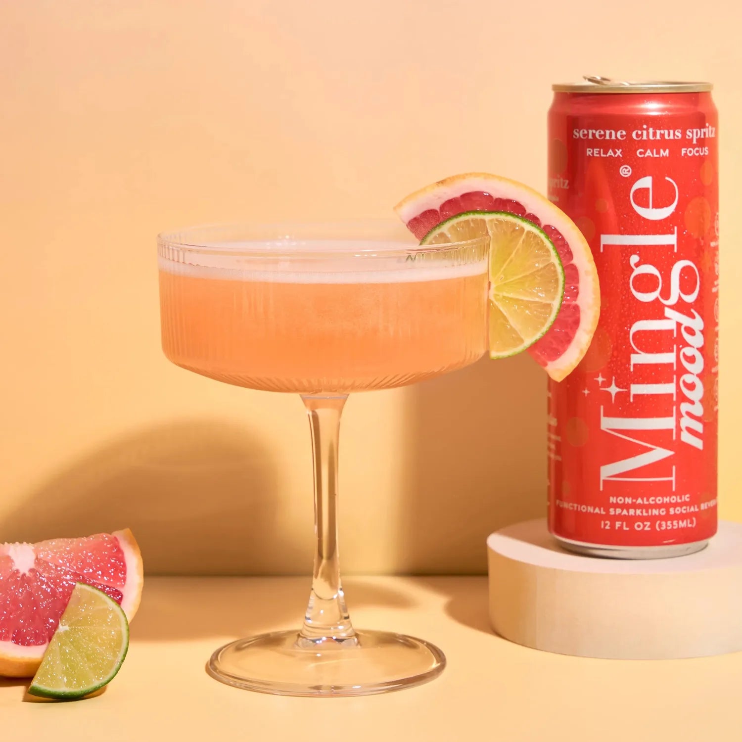 Mingle Mood Serene Citrus Spritz served in a coupe glass with grapefruit and lime garnish beside the coral can on a peach background.